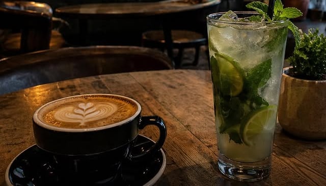 Latte and a mojito on a wooden table under the good coffee good mood neon sign